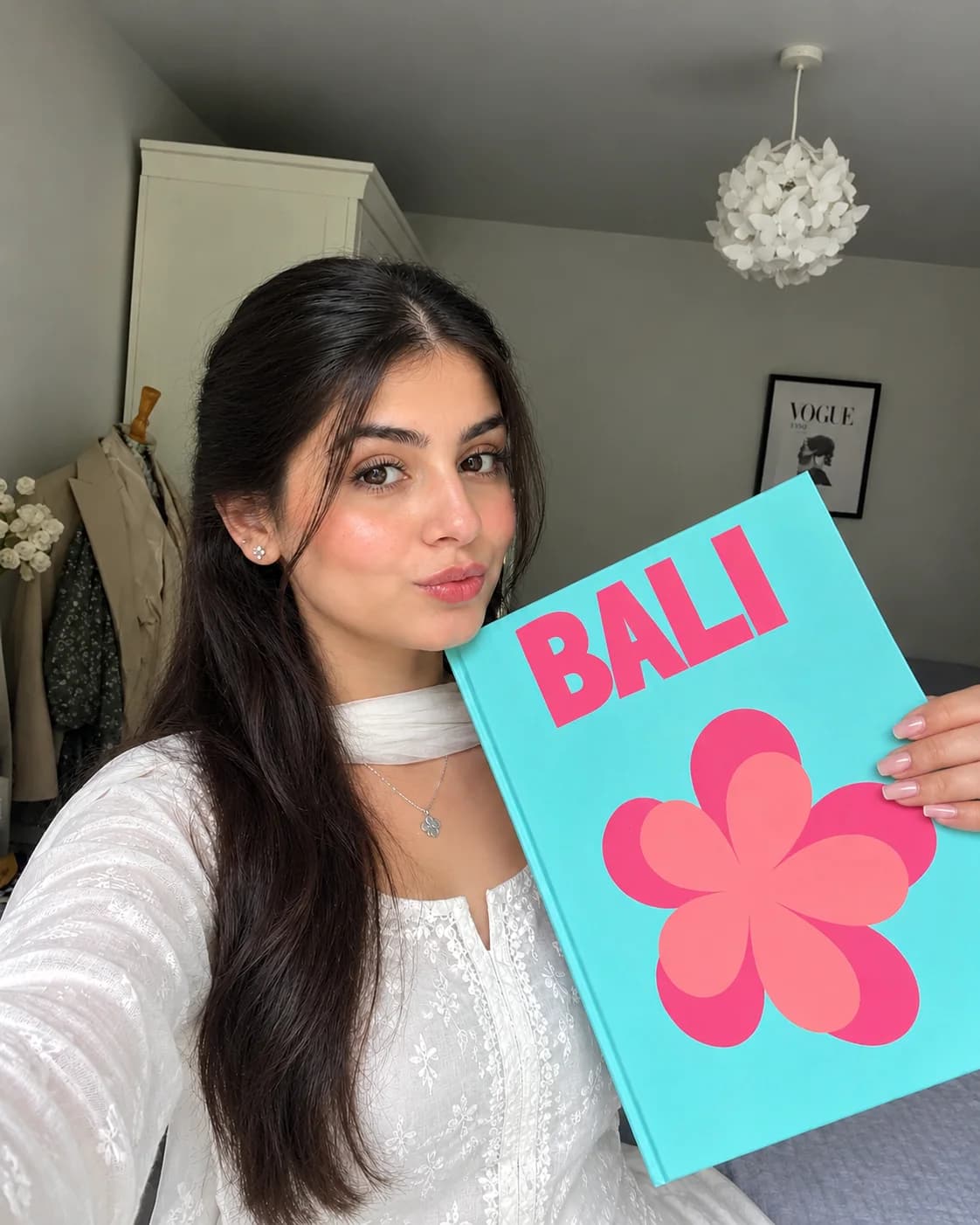 A girl in a white kurta holding a turquoise Bali photobook with a pink flower on it