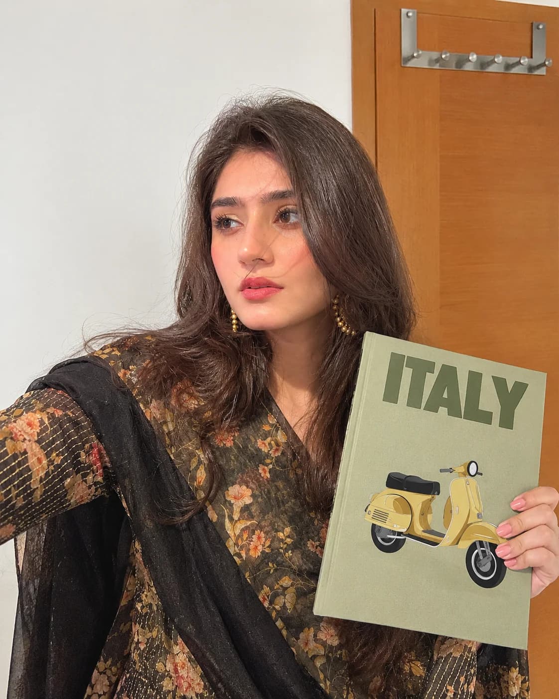 A girl in an embroidered kurta holding a sage green Italy photobook